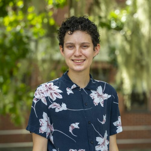 Quinn smiling facing the camera for a headshot in front of Dickinson Hall greenery.