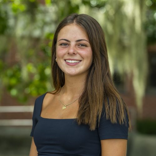 Grace smiling in front of greenery at Dickinson Hall for headshot.