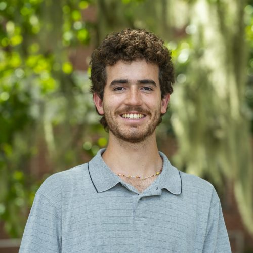 Tommy facing the camera, smiling for a headshot in front of Dickinson Hall greenery.