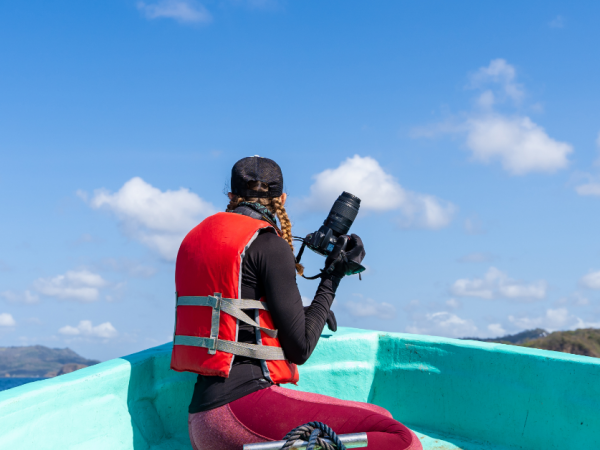 someone sitting on the front edge of a canoe wearing a life jacket and holding a camera to produce a documentary about the ocean