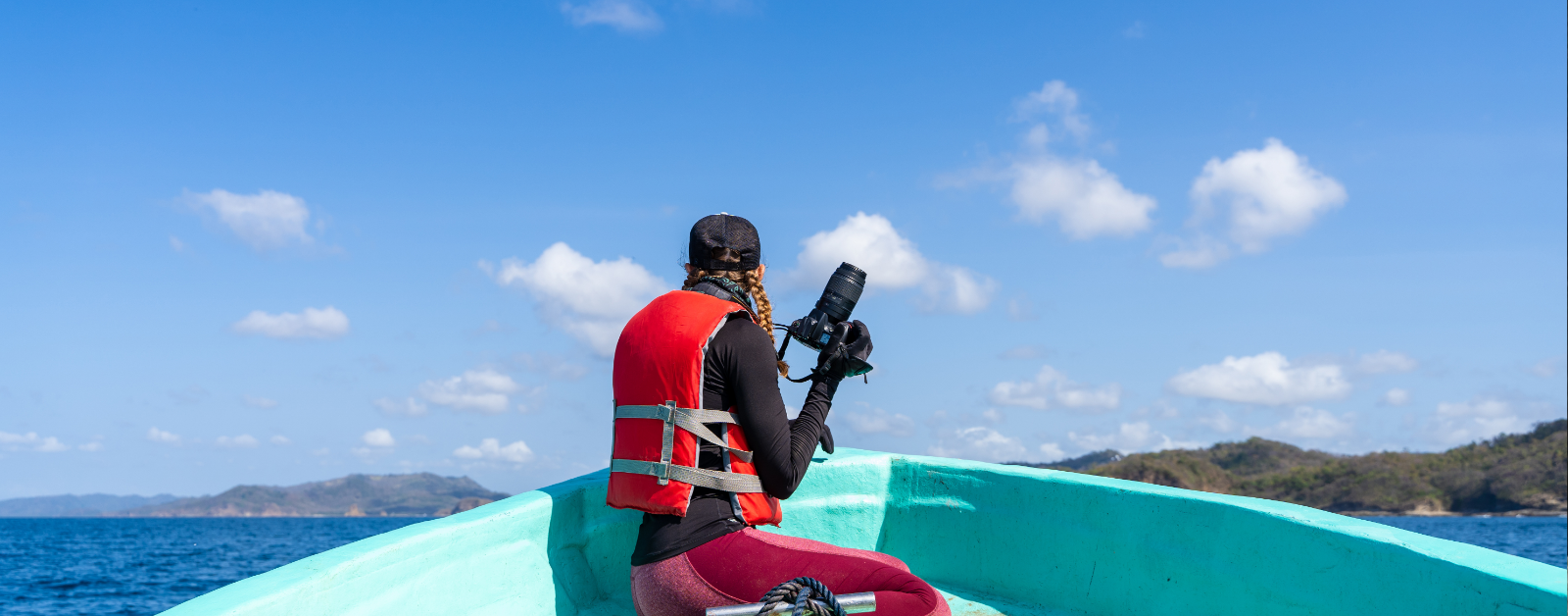 someone sitting on the front edge of a canoe wearing a life jacket and holding a camera to produce a documentary about the ocean