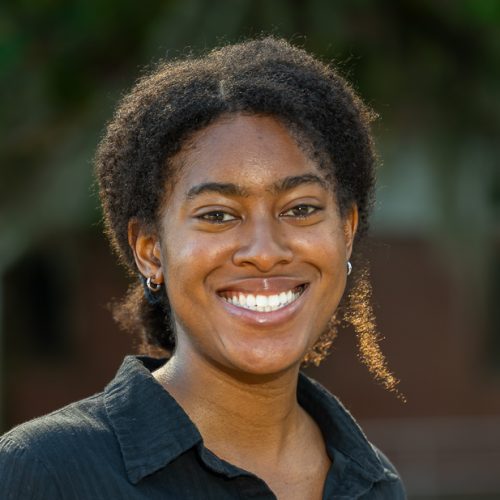 Azhalia Pottinger wearing a black button-up standing outside of Dickinson Hall and smiling for a headshot.