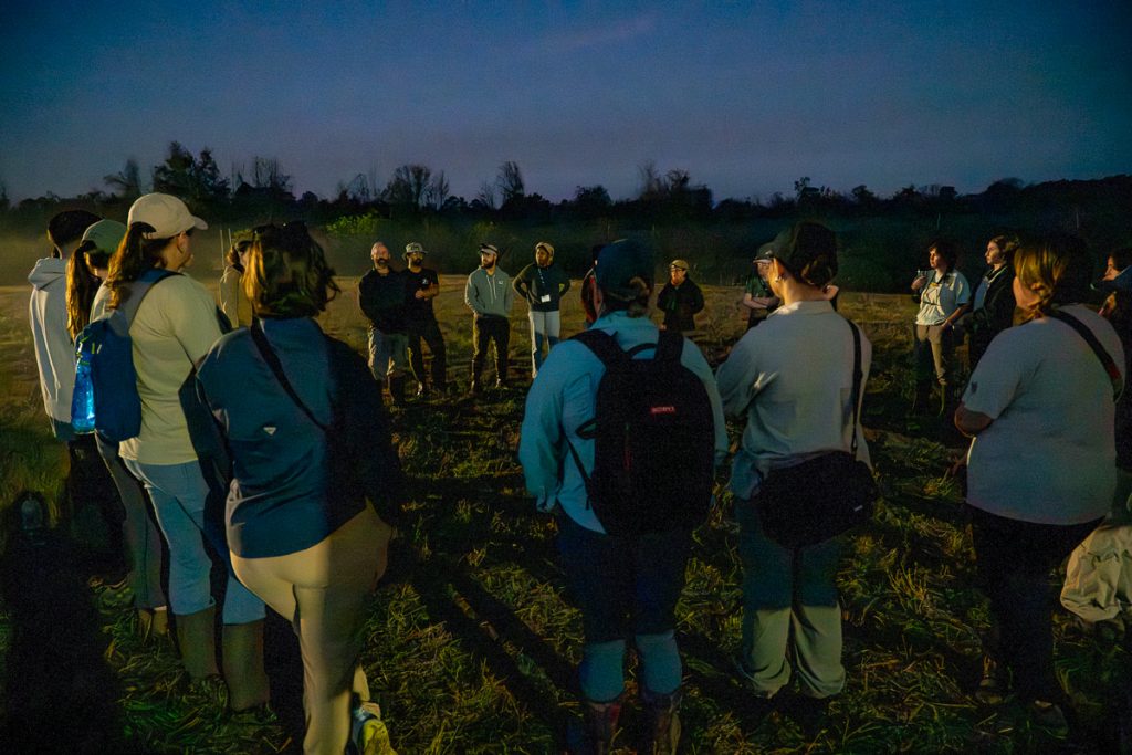 TESI ELF fellows and banding volunteers stand in a circle to listen to Charlie Muise