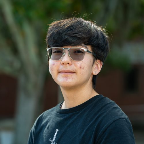 Eva Poore wearing a black t-shirt standing outside of Dickinson Hall and lightly smiling for a headshot.