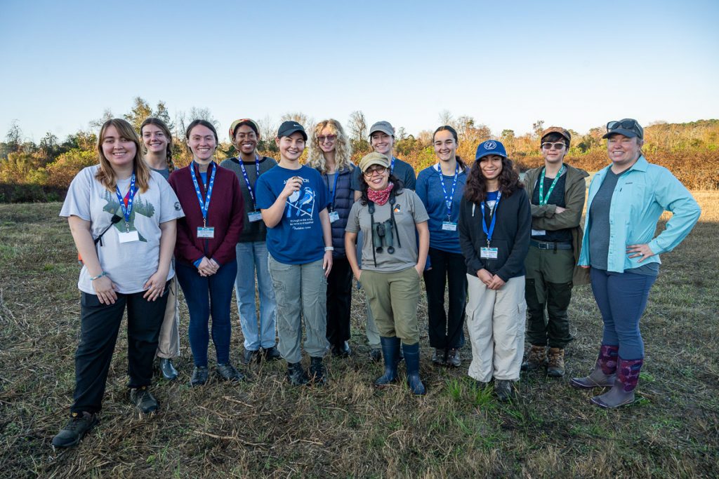 ELF fellows stand for group photo with Glaucia Del-Rio. Elle Henson holds a Marsh Wren at the front.
