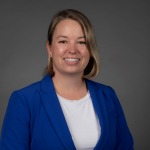 Megan Ennes headshot with blue blazer and gray background.