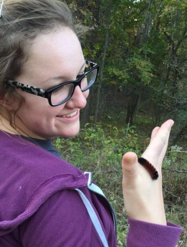 Scientist looking at a caterpillar on her hand and smiling.